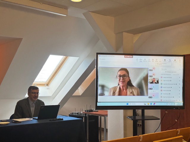 Siedzący mężczyzna oraz kobieta na ekranie telewizora